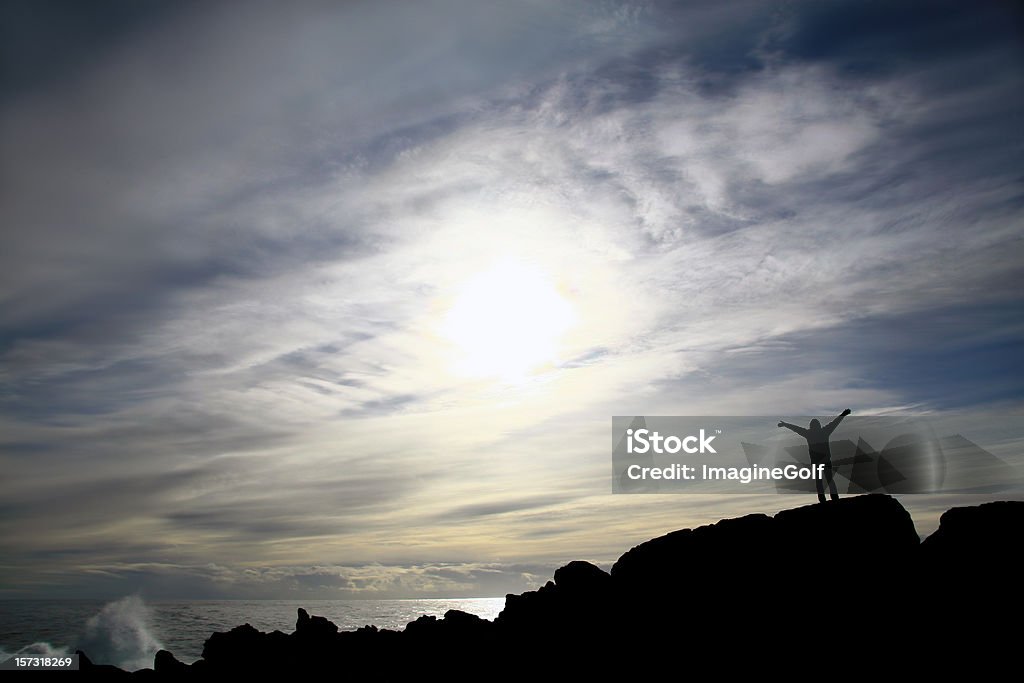 Woman Standing by the Sea with Arms Raised A silhouete of a woman standing by the sea. Image location is near Tofino, British Columbia, Canada along the Pacific Ocean. Back view. Woman in her 30s is unrecognizable. Tofino is on Vancouver Island and is famous for its storm watching as massive storm regions reach this coastline unimpeded by any other land masses.  Arms Raised Stock Photo