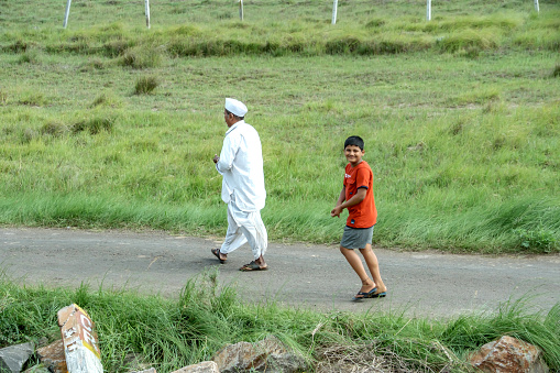Pune, India - July 23 2023: Portrait of a young Indian kid walking with an elderly man at a village near Pune India.