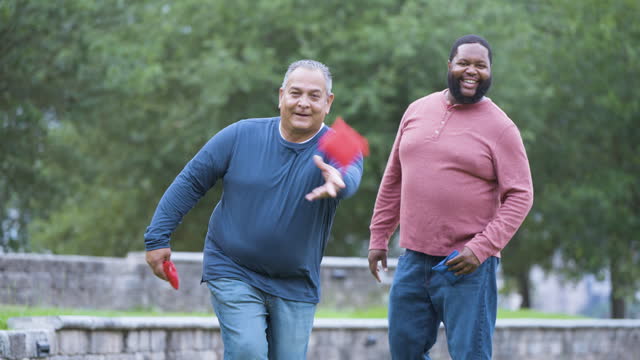 Two heavyset multiracial men playing bean bag toss