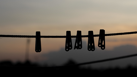 silhouette of clothes hanger pin hanging on clothesline in the afternoon