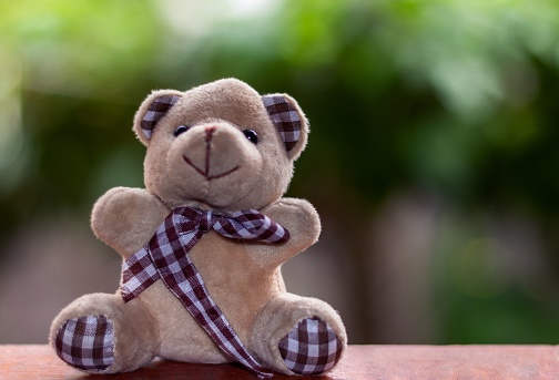 A cute, brown, stuffed teddy bear sits atop a wooden table with a bright ribbon