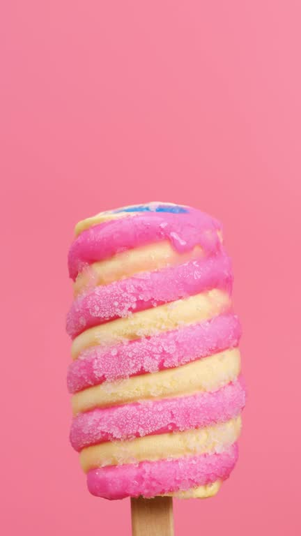 Multi-colored threaded stick popsicle melt on pink background.