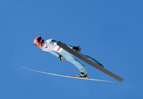 A male ski jumper crouches in position and gets ready to leap off a nordic ski jump.
