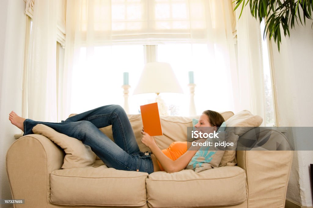 young brunette liest ein Buch auf dem sofa - Lizenzfrei Auf dem Rücken liegen Stock-Foto