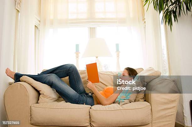 Young Brunette Liest Ein Buch Auf Dem Sofa Stockfoto und mehr Bilder von Auf dem Rücken liegen - Auf dem Rücken liegen, Frauen, Ganzkörperansicht