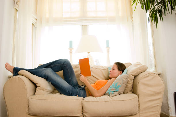 istock young brunette reading a book on the sofa 157327655