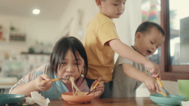 Joyful Sibling Bonding: Asian Brother and Sister Sharing Fun Spaghetti Moment at Home