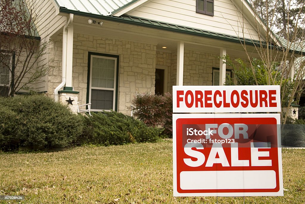 Foreclosure for sale sign in front of house White stone home with green roof and shrubbery in front.  A red and white sign in the foreground reads "Foreclosure - For Sale." Foreclosure Stock Photo