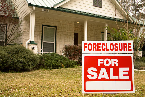 Foreclosure for sale sign in front of house White stone home with green roof and shrubbery in front.  A red and white sign in the foreground reads "Foreclosure - For Sale." foreclosure photos stock pictures, royalty-free photos & images