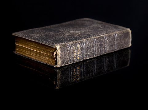 An antique bible on a black reflective surface.