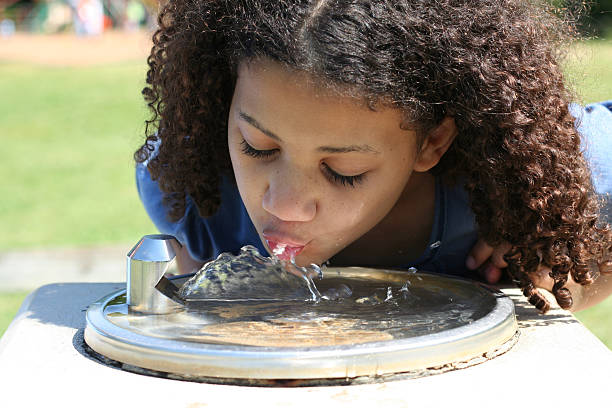 A girl taking a sip from a water dispenser at a park Little girl at a drinking fountain outside drinking fountain stock pictures, royalty-free photos & images