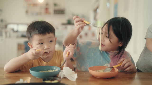 Cherishing Togetherness: Happy Asian Siblings Enjoying Spaghetti Meal with Laughter.