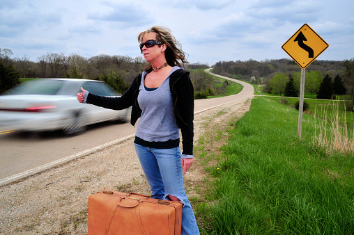 A woman hitchhiking with a car whizzing by.
