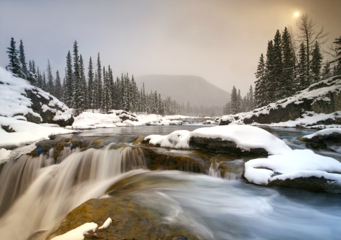 A winter scenic. Long exposure of waterfall. Alberta, Canada. Elbow Falls, Kananaskis Country. Snowy landscape. This gorgeous waterfall is located just an hour west of Calgary in the Canadian Rockies. Beautiful winter landscape with snow, ice, water, and sun shining through the mist on a cold January evening. Nobody is in the image, which was taken with a Canon 5D Mark II body and L series lens with a one-stop neutral density grad filter. 