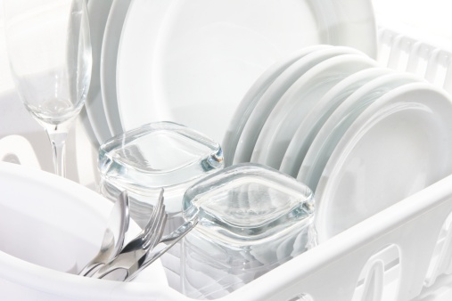 Closeup of White dishes drying on a rack.  There is a hint of colour in this image, including faint blue highlights.
