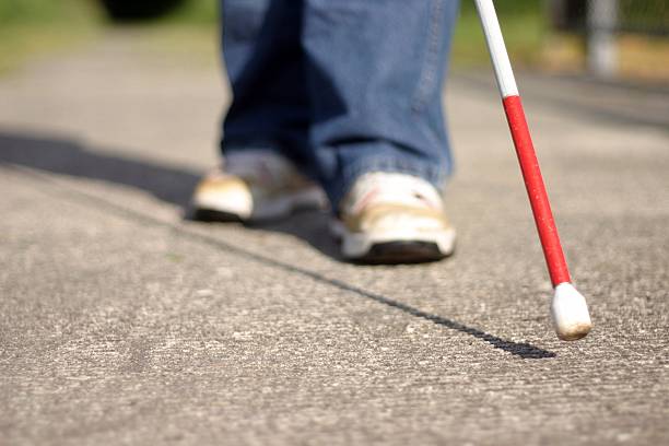 Cane Tip and Feet A young cane user feels his way along the sidewalk. Selective focus: Cane in in focus, feet out of focus. blind persons cane stock pictures, royalty-free photos & images