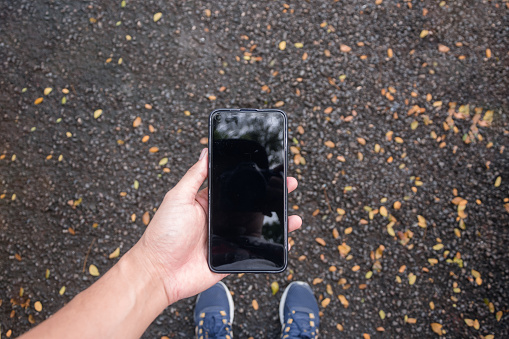 Personal perspective view of man hand holding a phone while walking on the sidewalk