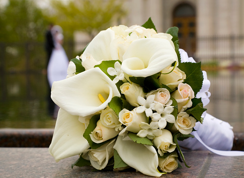 A wedding bouquet with the bride and groom in the out of focus background.