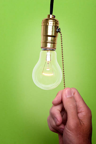 Hand pulling chain to turn off light bulb green background Hanging light bulb with pull switch.  Person is turning on or off the light.  Can see glowing filament. gchutka stock pictures, royalty-free photos & images