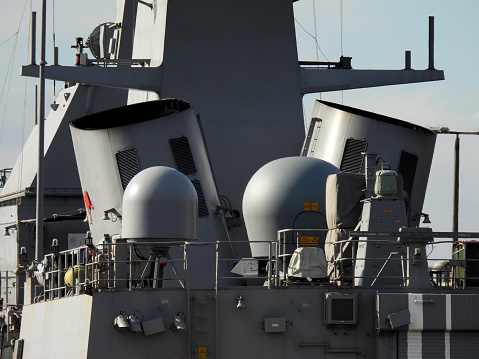 The funnels, mast and radar domes of HMAS Warramunga (FFH 152), an Anzac Class frigate of the Royal Australian Navy (RAN), is docked at Garden Island naval base in Sydney Harbour.  The RAN insignia of a red kangaroo is affixed to her left funnel.  This image was taken from Woolloomooloo Bay on a sunny afternoon on 22 July 2023.