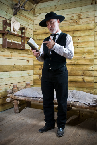 Preacher standing alone in his simple wooden bedroom reading the bible, pointing with his finger to a bible page.
