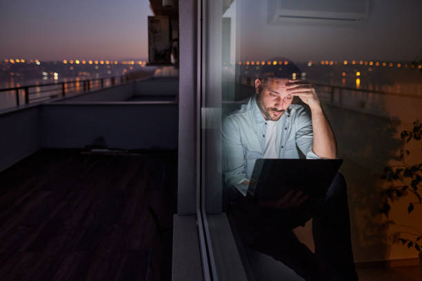 hombre preocupado usando la computadora portátil junto a la ventana por la noche. - looking through window businessman problems reading fotografías e imágenes de stock