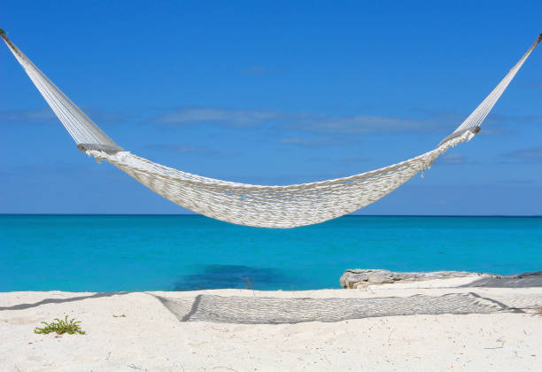 White hammock over a white sand beach with bright blue sky stock photo