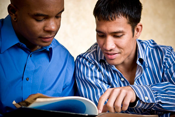 Two men reading a book with one pointing at page