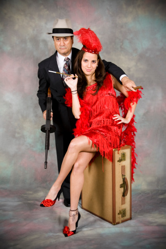 Gangster with machine gun and his woman.  She sits on an old suitcase.