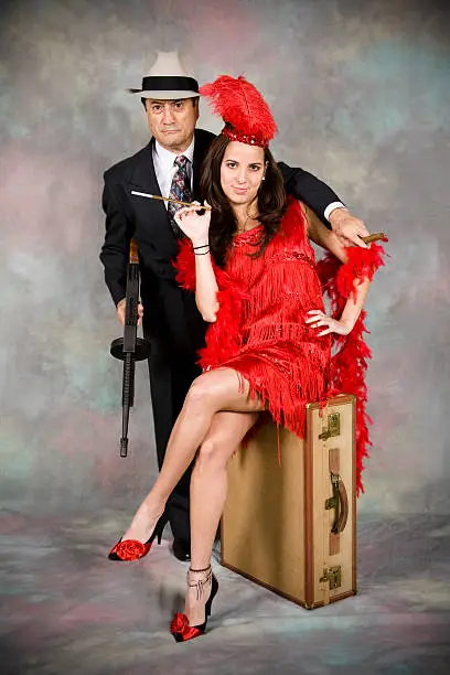 Gangster with machine gun and his woman.  She sits on an old suitcase.