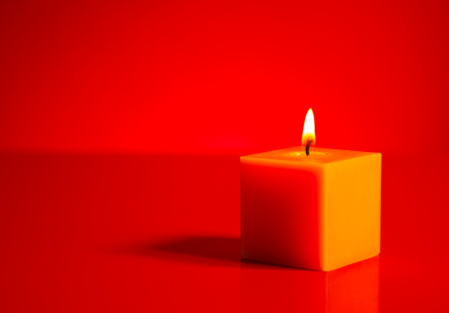 Burning yellow candle over the red background