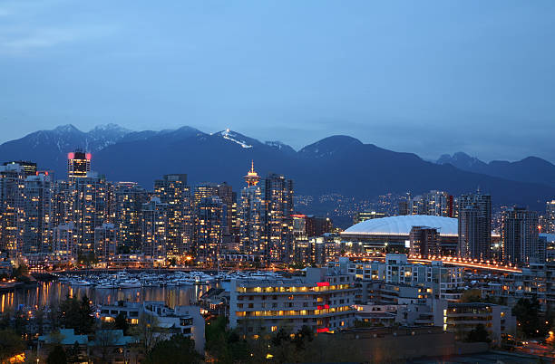 Vancouver Yaletown With Grouse Mountain Evening looking toward False Creek, Yaletown Seawalk,BC Place,and Cambie Street Bridge. North shore Mountains in Background with ski hill lite up. This is photographed in May.  false creek stock pictures, royalty-free photos & images