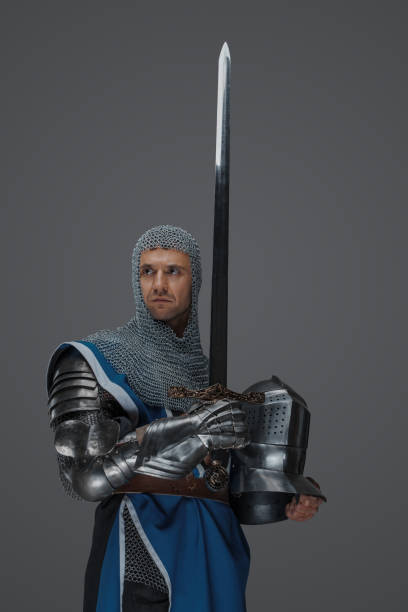 Proud knight stands holding his sword and helmet
