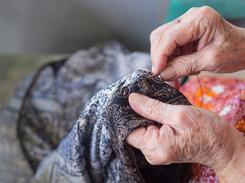 Close-up of elderly woman hands using needle and thread to mend a pants. Selective focus.