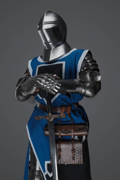 istock Medieval guard dressed in armor and blue surcoat holding a sword 1573388988