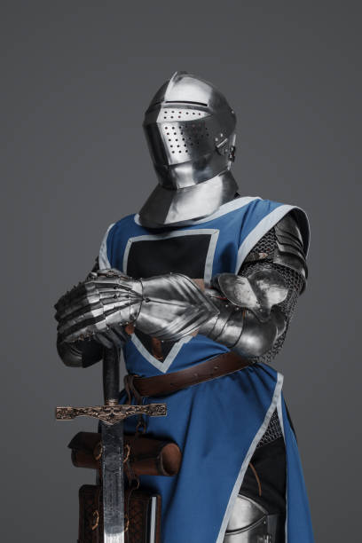 istock Medieval guard dressed in armor and blue surcoat holding a sword 1573390009