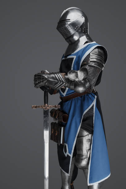 istock Medieval guard dressed in armor and blue surcoat holding a sword 1573391039