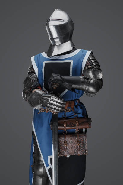 istock Medieval guard dressed in armor and blue surcoat holding a sword 1573392073