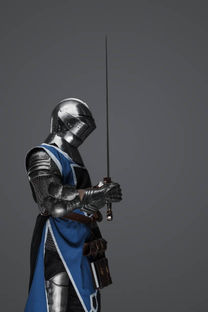 istock Medieval guard dressed in armor and blue surcoat holding a sword 1573393635