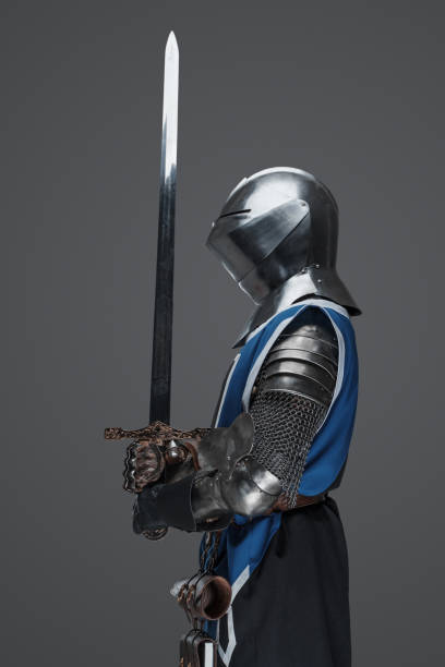 istock Medieval guard dressed in armor and blue surcoat holding a sword 1573394722