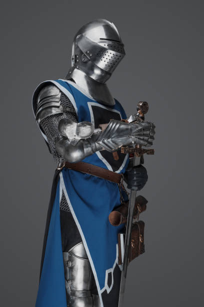 istock Medieval guard dressed in armor and blue surcoat holding a sword 1573395305