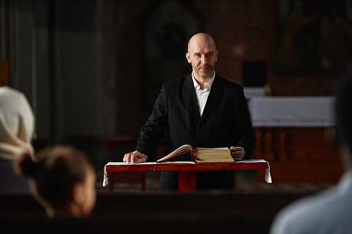 Mature pastor reading Bible for believers while standing at altar in church