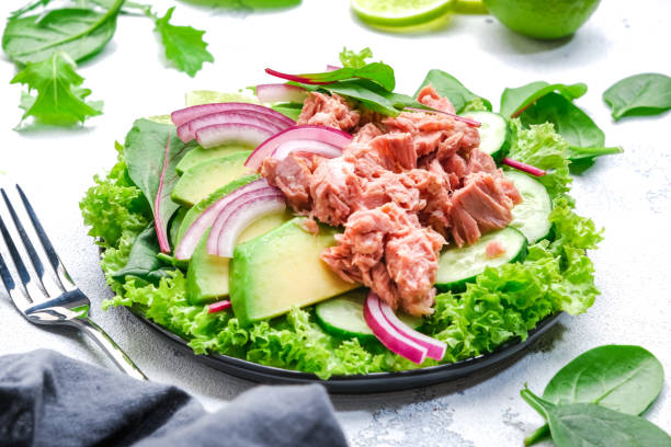 istock Canned tuna salad with avocado, cucumber, onion, spinach, lettuce and lime. White table background, top view 1573412002