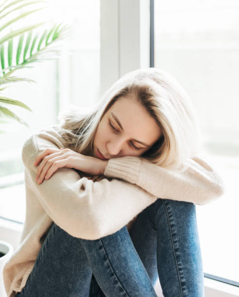istock Sad girl near window thinking about something 1573432119