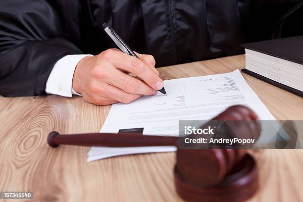 Male Judge Signing Papers With A Gavel In Front Of Him Stock Photo - Download Image Now