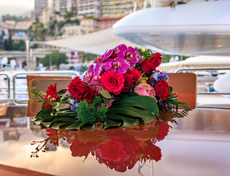 Beautiful live flower arrangement of orchids and roses on a luxury yacht with blurred Monte Carlo, Monaco cityscape in the background at sunset