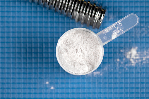 Scoop with white powder protein or gainer as the sports nutrition on blue mat at a gym