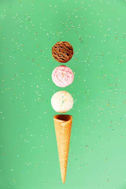 istock Chocolate, vanilla, strawberry scoops and waffle cone on green background with colorful sprinkles, levitating concept 1573500095