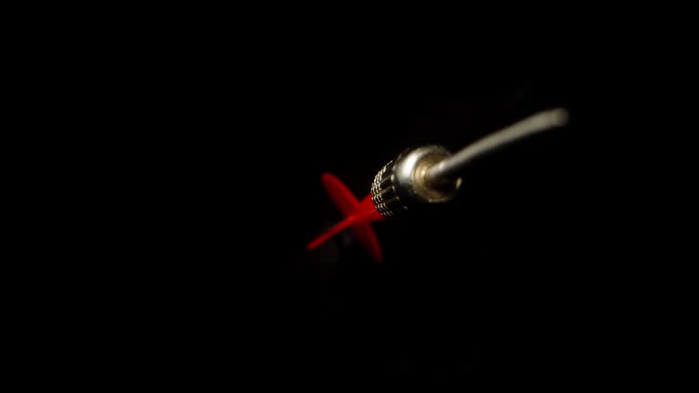 The red dart for darts rotates and flies on a black background, Slow-motion macro.