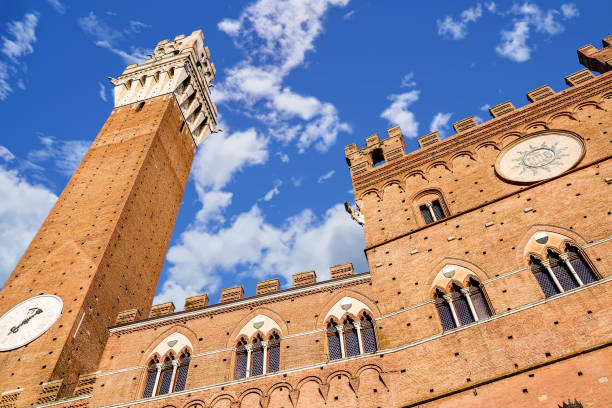 A view from below of the Palazzo Pubblico in the Piazza del Campo in the heart of Siena in Tuscany A suggestive view from below of the majestic Torre del Mangia (Mangia tower) and the Palazzo Pubblico (Public Building) in the Piazza del Campo, in the medieval heart of Siena, in Tuscany. Built in 1290 as the seat of the Council of Nine and of the executive power of the medieval city, the majestic Palazzo Pubblico is still the seat of the municipal government of Siena. The Torre del Mangia was built between 1338 and 1348 on a project by Giovanni Balduccio, known as the 'Mangia', becoming the symbol of the political and military power of Siena compared to its rival Florence. Center of the city life since 1169, Piazza del Campo or simply Campo is one of the most beautiful and famous squares in the world for its particular shell shape. In this space every year the seventeen historical districts of Siena compete in the Palio, one of the oldest horse races in the world. Siena is one of the most beautiful Italian cities of art, in the heart of the Tuscan hills, visited for its immense artistic and historical heritage and for its famous popular traditions. Since 1995 the historic center of Siena has been declared a World Heritage Site by UNESCO. Image in high definition quality. torre del mangia stock pictures, royalty-free photos & images